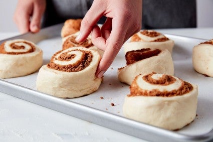 Baker using poke test on proofing cinnamon rolls